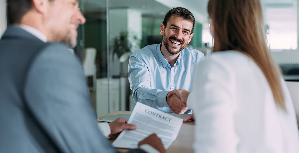 Vier Personen gehen gemeinsam eine gl&auml;serne Treppe hinunter und unterhalten sich in einem lichtdurchfluteten B&uuml;rogeb&auml;ude.