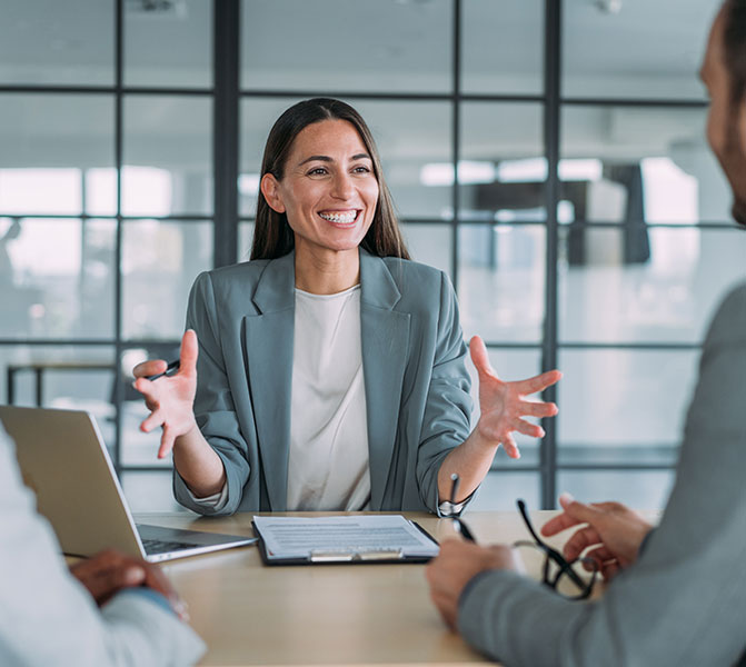 Eine Frau spricht l&auml;chelnd mit zwei Kollegen in einem modernen Besprechungsraum.