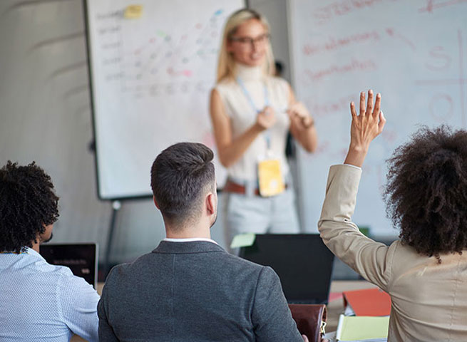 Eine Frau steht vor einem Whiteboard und erkl&auml;rt etwas einer Gruppe von Teilnehmenden.