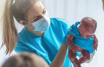 Hebamme h&auml;lt neugeborenes Baby nach der Entbindung.