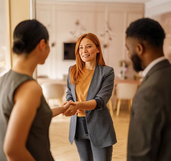 Drei Personen stehen in einem freundlich eingerichteten Raum, w&auml;hrend eine Frau einer Bewerberin die Hand sch&uuml;ttelt &ndash; Symbol f&uuml;r ein erfolgreiches Bewerbungsgespr&auml;ch.
