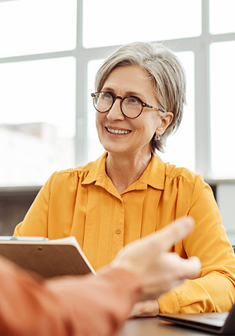 Frau in orangener Bluse beim Bewerbungsgespr&auml;ch
