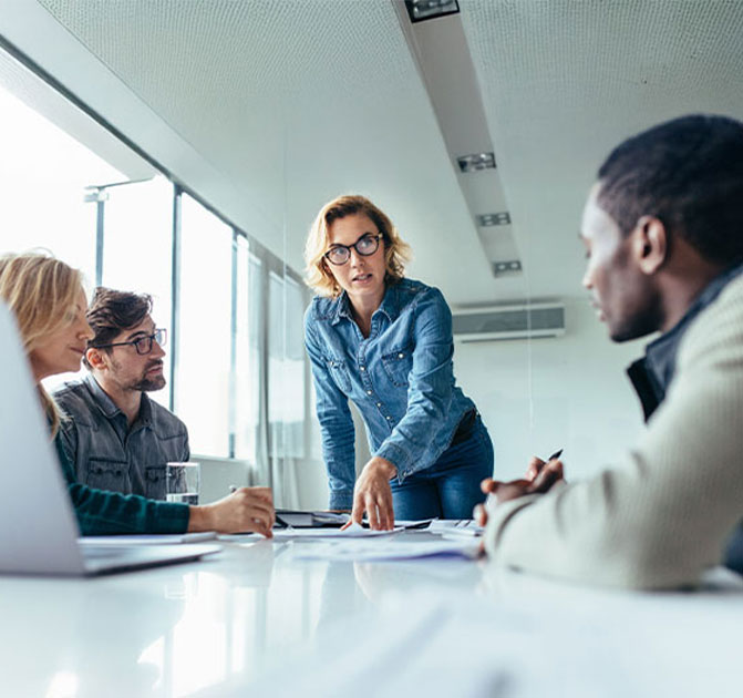 Vier Personen sitzen an einem Konferenztisch und besprechen Bau- oder Projektpl&auml;ne in einem modernen B&uuml;ro.