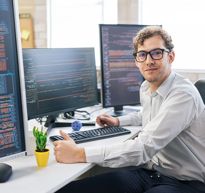 Ein Programmierer sitzt am Schreibtisch vor zwei Monitoren mit Code und arbeitet konzentriert.