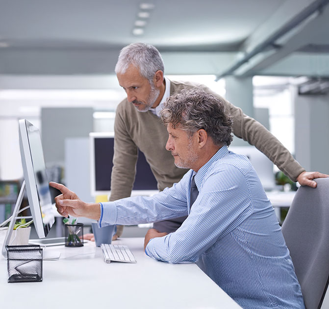 Zwei M&auml;nner arbeiten gemeinsam an einem Bildschirm und besprechen technische Details in einem hellen B&uuml;ro.