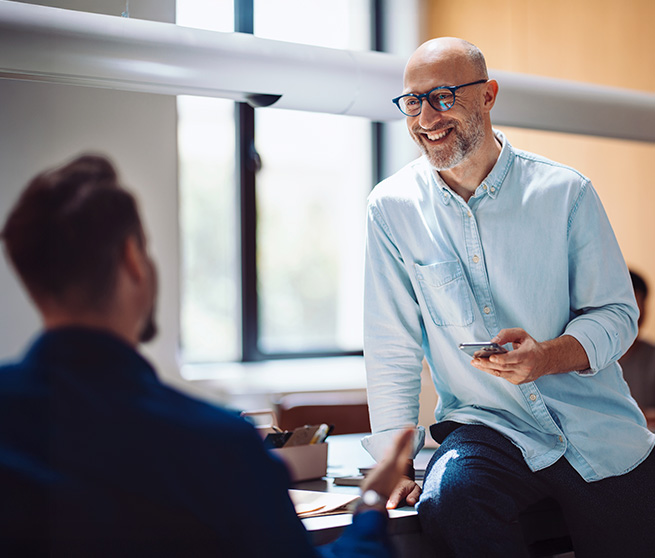Entspannter Mann mit Brille unterh&auml;lt sich freundlich mit einem Kollegen im B&uuml;ro.