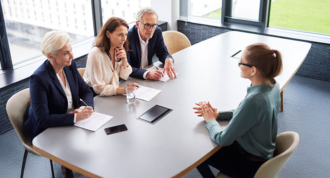 Drei Recruiter f&uuml;hren ein Gespr&auml;ch mit einer Bewerberin in einem hellen Meetingraum.