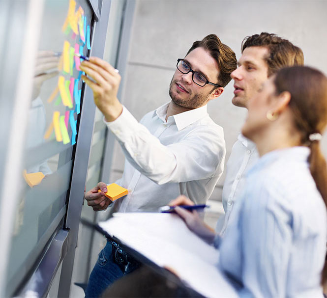 Zwei Kollegen entwickeln gemeinsam Ideen an einer Pinnwand mit bunten Notizzetteln.