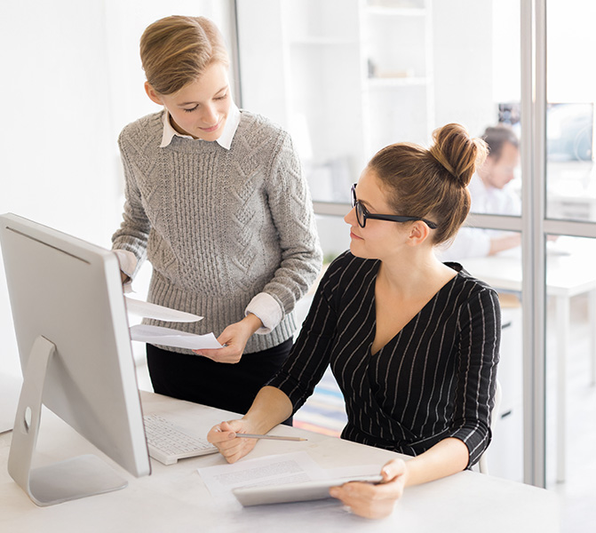 Zwei Mitarbeiterinnen im B&uuml;ro arbeiten gemeinsam am Computer und besprechen Unterlagen.