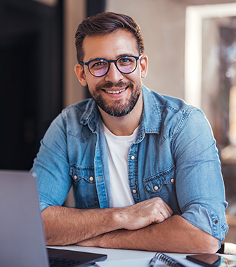 Gesch&auml;ftsmann mit Brille arbeitet l&auml;chelnd am Laptop in modernem B&uuml;ro.