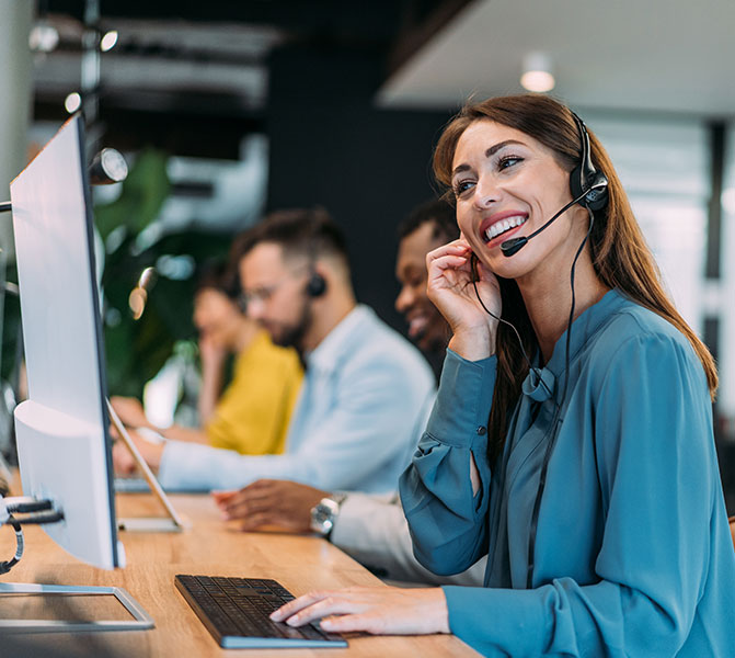 Eine l&auml;chelnde Frau mit Headset arbeitet an einem Computer in einem modernen B&uuml;ro.