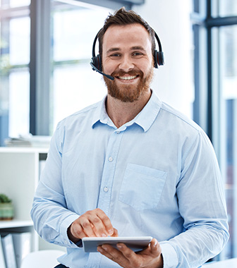 Freundlicher Callcenter-Mitarbeiter mit Headset und Tablet l&auml;chelt im B&uuml;ro.