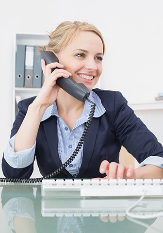 Eine Frau sitzt an ihrem Arbeitsplatz, telefoniert l&auml;chelnd und tippt gleichzeitig auf ihrer Tastatur.