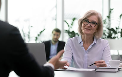Eine Frau mit Brille f&uuml;hrt ein professionelles Gespr&auml;ch an einem Schreibtisch in einem modernen B&uuml;ro.