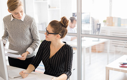 Zwei Kolleginnen besprechen Unterlagen am Arbeitsplatz im modernen B&uuml;ro.