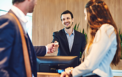 Mitarbeiter am Empfang begr&uuml;&szlig;t freundlich G&auml;ste und &uuml;bergibt eine Schl&uuml;sselkarte.