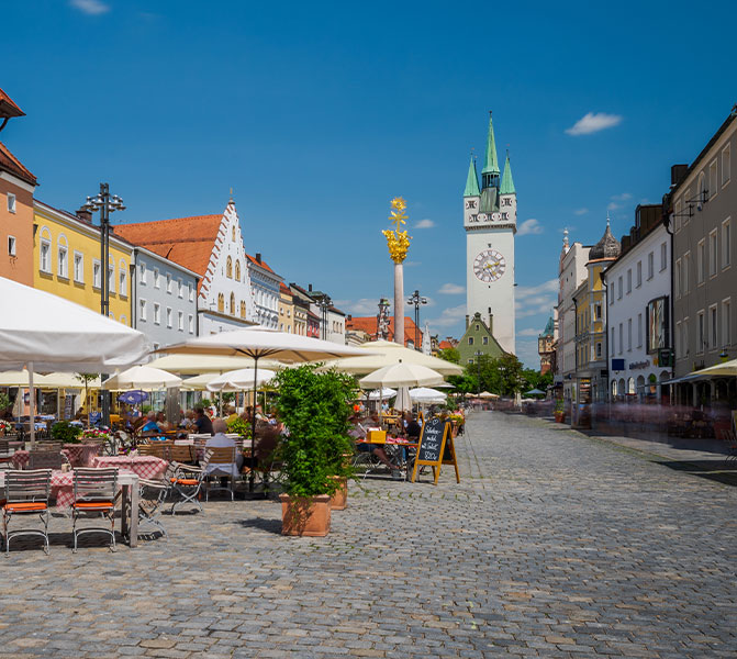 Blick auf den historischen Marktplatz in Straubing mit Restaurants und Uhrturm.