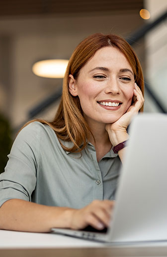 Junge Frau arbeitet motiviert am Laptop und l&auml;chelt w&auml;hrend eines Videocalls im B&uuml;ro.