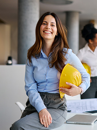 L&auml;chelnde Frau mit Helm an einem Schreibtisch