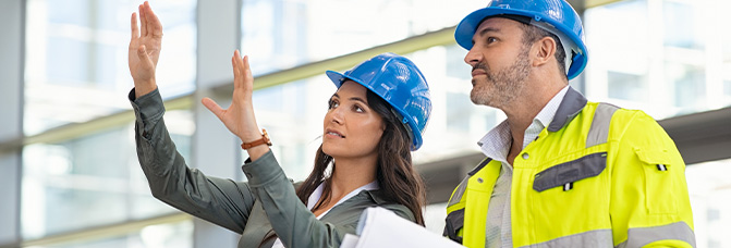 Man und Frau mit Helm besprechen eine Baustelle vor Ort