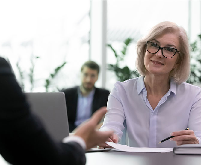 Eine Frau mit Brille f&uuml;hrt ein professionelles Gespr&auml;ch an einem Schreibtisch in einem modernen B&uuml;ro.