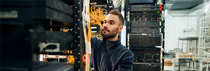 Techniker arbeitet konzentriert im Serverraum und &uuml;berpr&uuml;ft Kabel und Hardware.