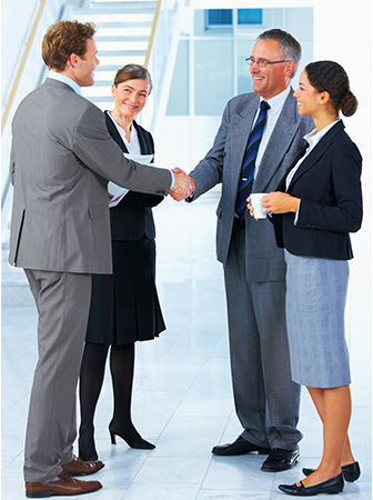 Gesch&auml;ftspartner sch&uuml;tteln sich die Hand, w&auml;hrend zwei weitere Kolleginnen l&auml;cheln &ndash; erfolgreicher Gesch&auml;ftsabschluss.