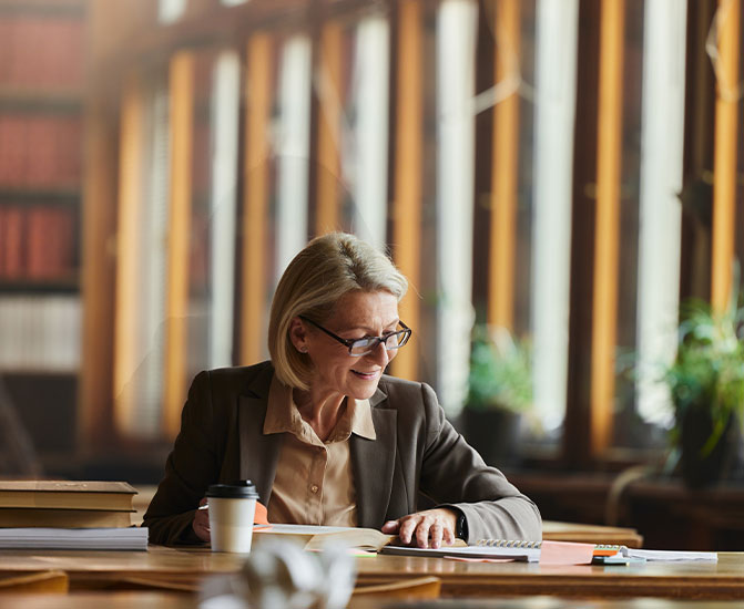 Juristin sitzt am Schreibtisch mit Unterlagen und arbeitet konzentriert in einer modernen B&uuml;roumgebung.