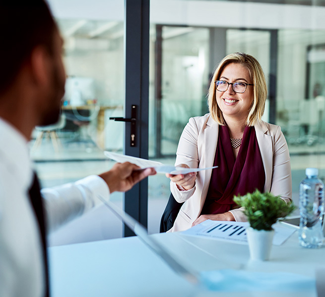 L&auml;chelnde Frau reicht einem Kollegen ein Blatt Papier in einem modernen Besprechungsraum.