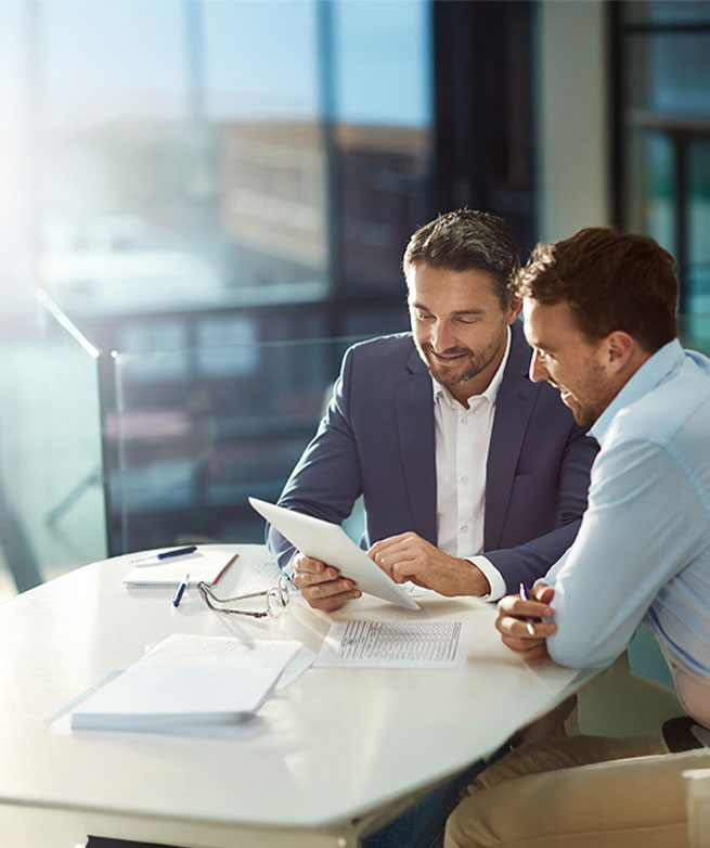 Zwei Gesch&auml;ftsm&auml;nner sehen gemeinsam auf ein Tablet und besprechen Recruiting-Strategien.