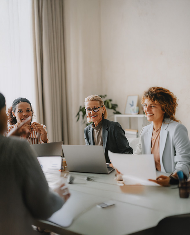 Drei Business-Frauen sitzen gemeinsam im Meeting und arbeiten an Laptops.