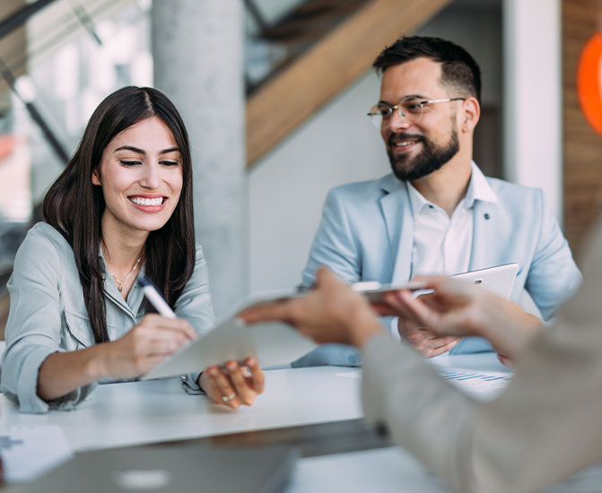 Zwei Personen sitzen an einem Tisch, l&auml;cheln und unterzeichnen gemeinsam ein Dokument.