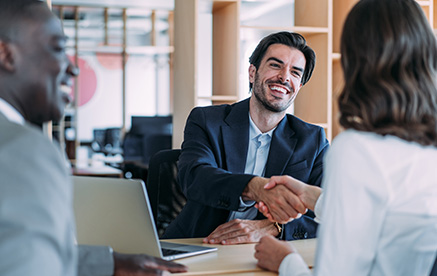 Gesch&auml;ftsmann l&auml;chelt und sch&uuml;ttelt einer Partnerin die Hand &ndash; erfolgreiche Zusammenarbeit.