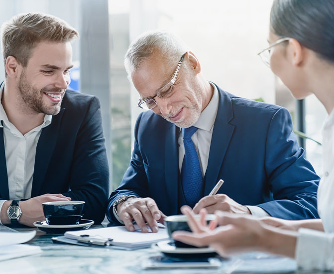 Senior Manager unterzeichnet im Meeting Dokumente, w&auml;hrend Kollegen zuh&ouml;ren.