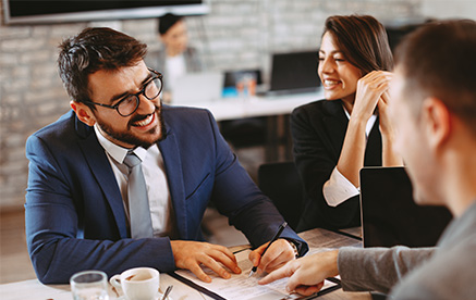 Gesch&auml;ftsmann bespricht Unterlagen mit Kollegen und l&auml;chelt w&auml;hrend des Gespr&auml;chs.