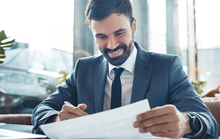 Gesch&auml;ftsmann im Anzug pr&uuml;ft Dokumente und l&auml;chelt zufrieden.